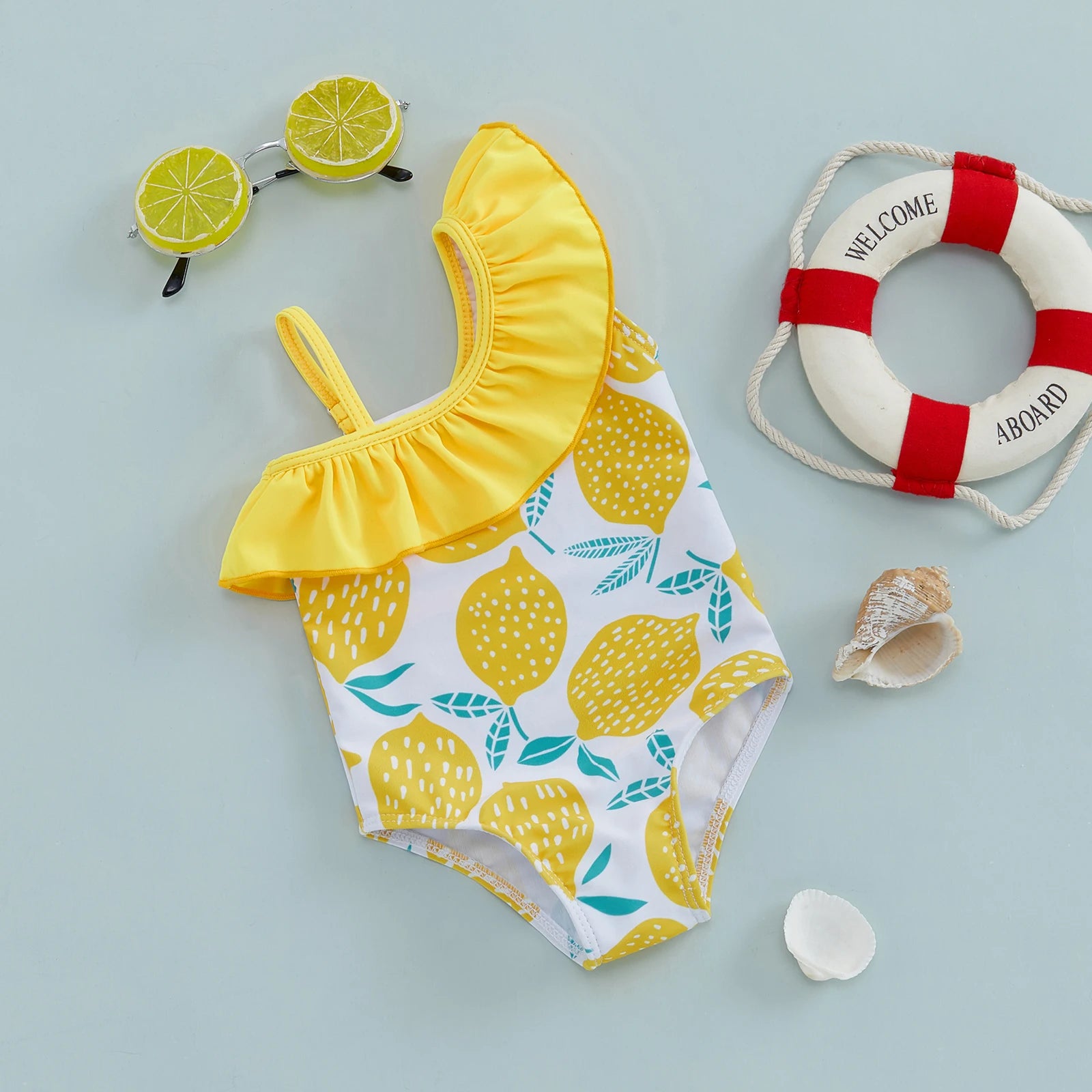 Baby girl wearing a lemon print one-shoulder swimsuit by Baby Bubble, bright and cheerful swimsuit for warm weather.