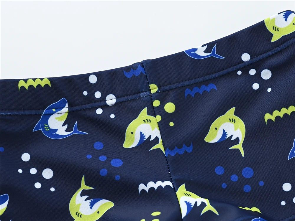 Boy wearing Baby Bubble boys' 2-piece swimsuit set with cool print, suitable for ages 1 to 7, shown on a sunny beach.