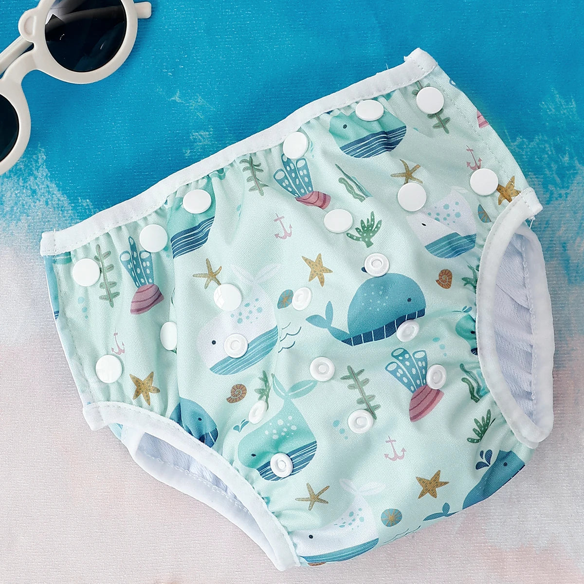 Baby Bubble washable and adjustable baby swim diapers shown in a colorful pool scene with a smiling baby wearing the diaper.